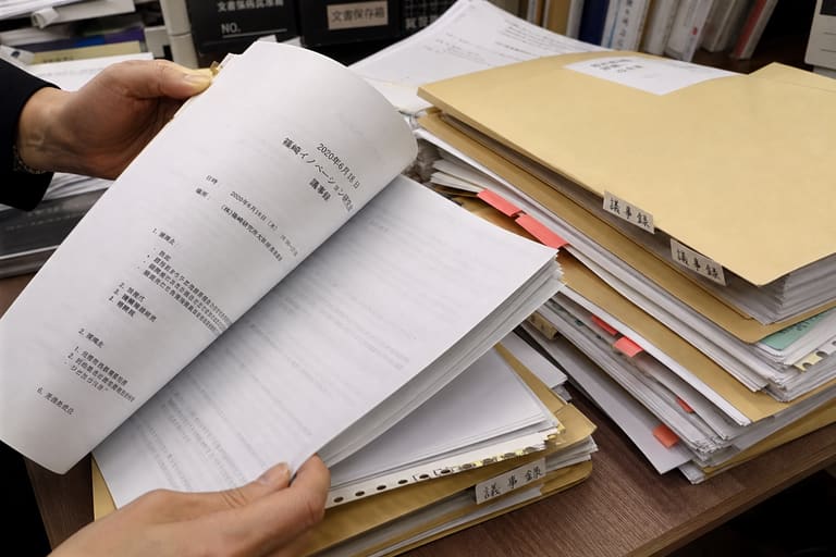 印刷された議事録の山を手作業で探す様子